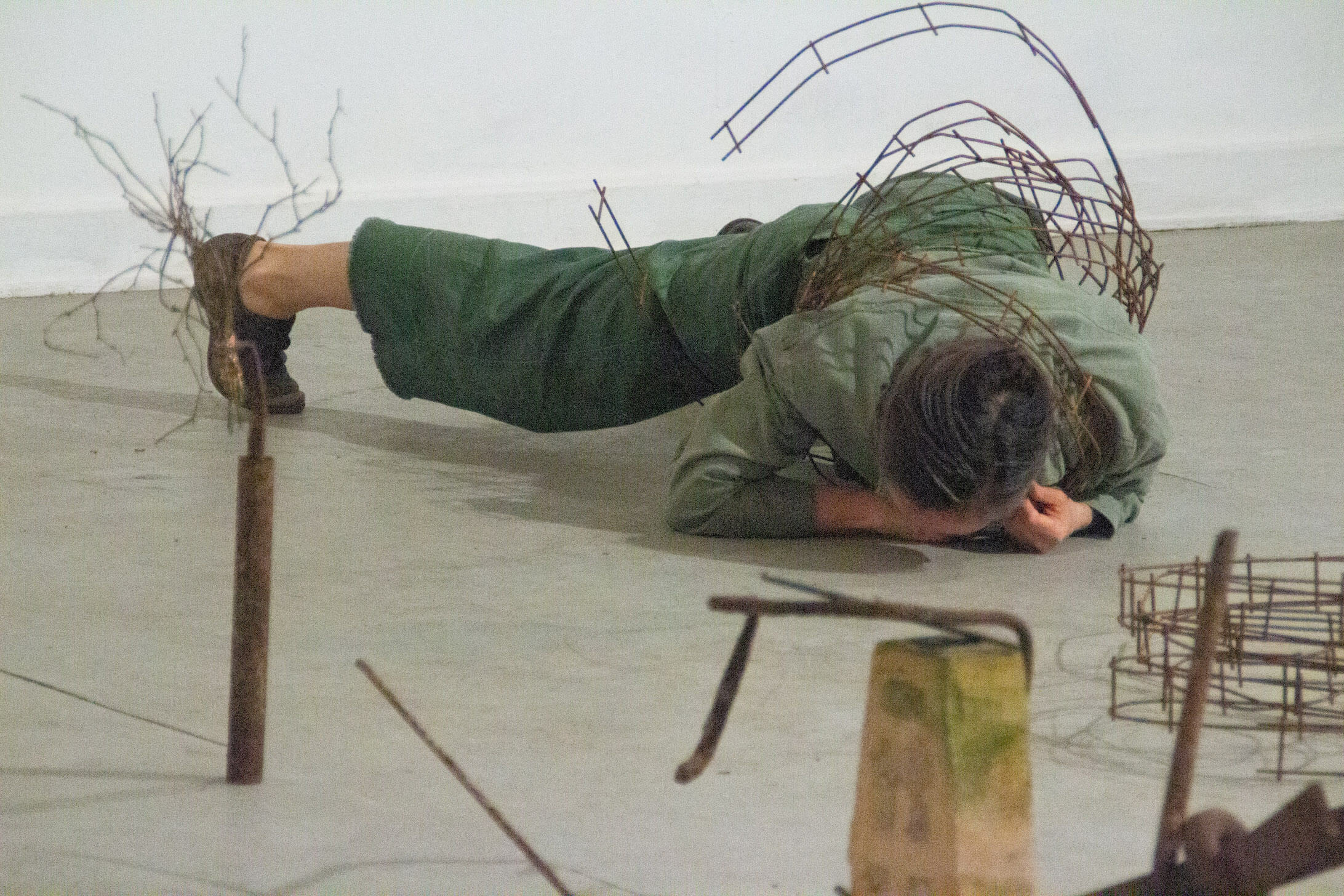 artist on ground with metal tracks wrapped around torso and objects surrounding her